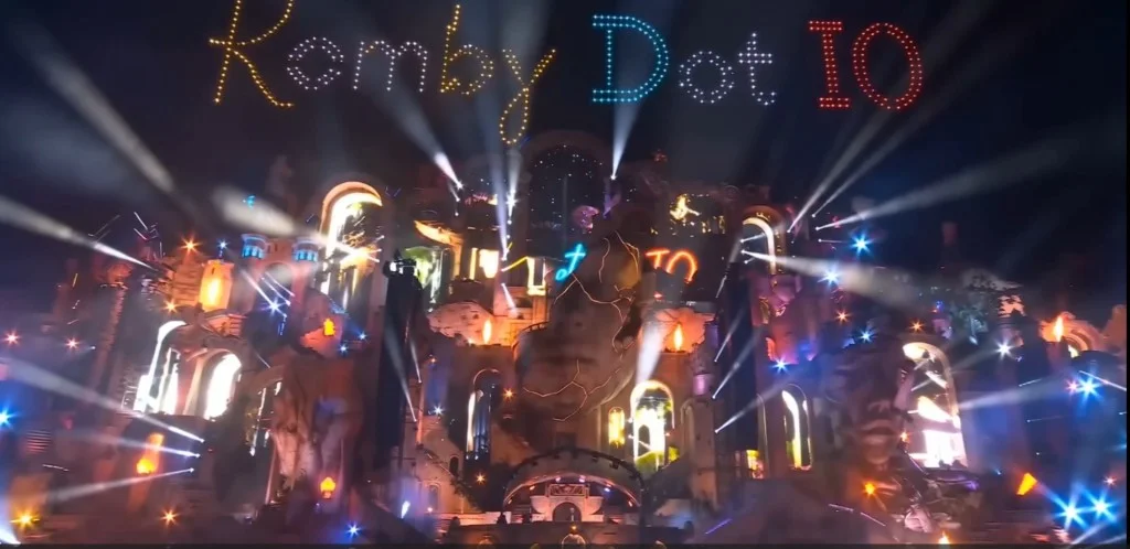 Illustration d’une scène monumentale de Komby Dot IO avec une architecture sculptée et un show de drones nocturne.