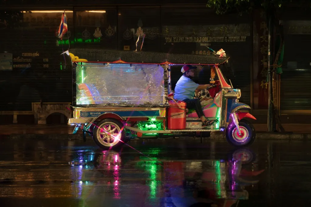 Tuk-tuk glowing with green and pink neon on a wet Bangkok street at night