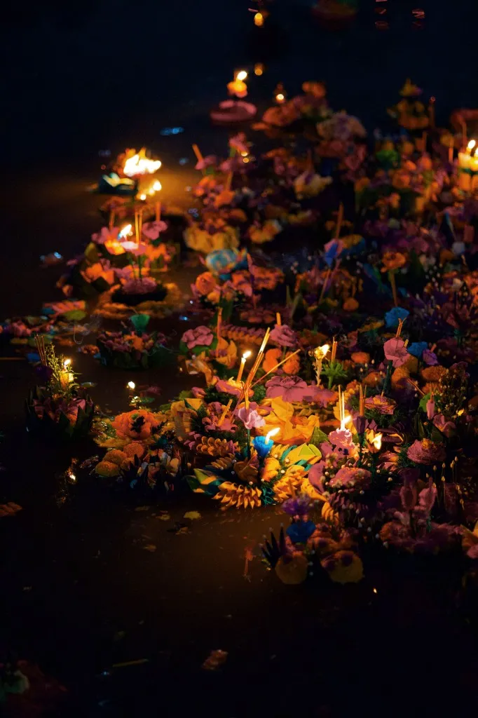 Flower krathongs and lit candles floating on the water during Loy Krathong in Thailand